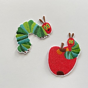 Könnte beinhalten: Zwei gestickte Aufnäher mit einer grünen, blauen und roten Raupe. Eine Raupe ist gebogen, die andere befindet sich auf einem roten Apfel. Die Aufnäher haben weiße Ränder und befinden sich auf weißem Hintergrund.