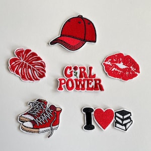 Könnte beinhalten: Eine Sammlung rot-weißer, gestickter Aufnäher. Designs umfassen eine Baseballkappe, Lippen, ein Blatt, ein Paar Turnschuhe, die Worte "GIRL POWER", ein Herz und einen Stapel Bücher. Diese Aufnäher sind ideal zum Dekorieren von Kleidung oder Accessoires.