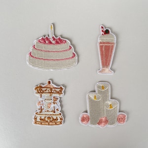 May include: Embroidered patches depicting a layered cake with a candle, a milkshake with a cherry, a carousel, and three candles with pink roses. The patches have a stitched border on a white background.