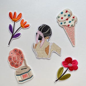 Op de afbeelding: Set van vijf geborduurde patches met diverse ontwerpen. Inclusief een bloem met oranje bloemblaadjes, een figuur met zwart haar, een ijsje, een vintage radio en een rode bloem.
