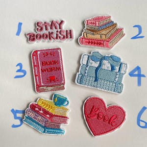 May include: Embroidered patches with book-themed designs. Includes patches with the phrases "Stay Bookish" and "Book Worm", stacks of books, and a heart-shaped patch with the word "Book". The patches feature various colours including pink, blue, yellow, and white.