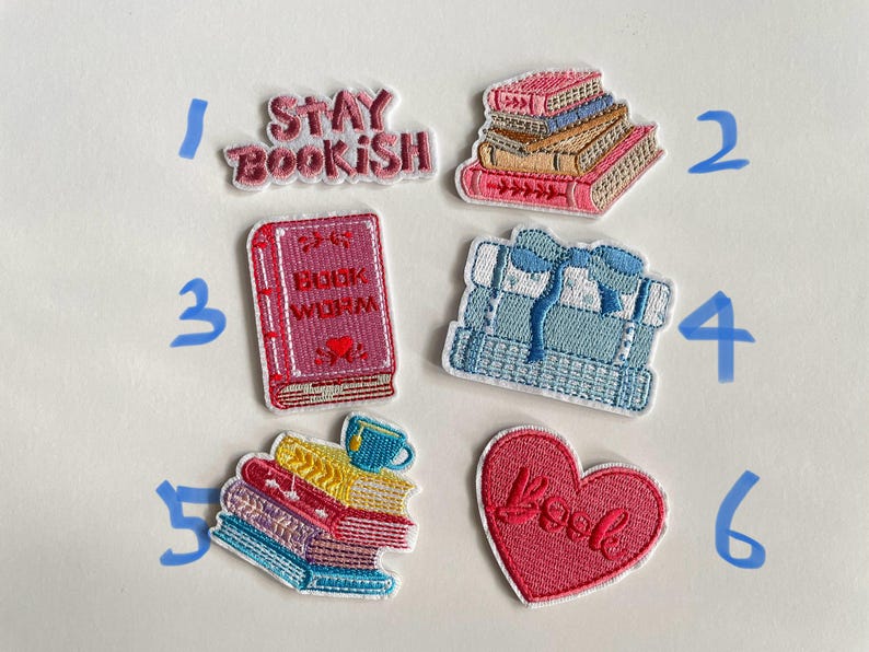 May include: Embroidered patches with book-themed designs. Includes patches with the phrases "Stay Bookish" and "Book Worm", stacks of books, and a heart-shaped patch with the word "Book". The patches feature various colours including pink, blue, yellow, and white.