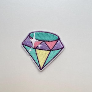 May include: Embroidered diamond patch in shades of teal, purple, pink, and yellow, with a white outline. The patch features a sparkling star design in the center, adding a touch of glamour. This patch is perfect for adding to clothing or accessories.