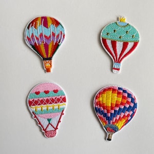 May include: Four embroidered hot air balloon patches in various colours. One balloon features red, yellow, and purple, another has teal and red stripes, a third is pink with hearts, and the last is blue, yellow, and orange.