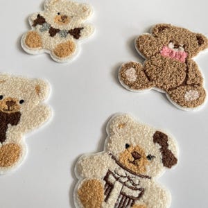 Pode incluir: Quatro patches bordados de ursinhos em v&aacute;rias cores. Dois s&atilde;o creme com detalhes marrons, um com um cachecol. Um &eacute; marrom com um la&ccedil;o rosa. O &uacute;ltimo &eacute; creme com um la&ccedil;o marrom e azul.