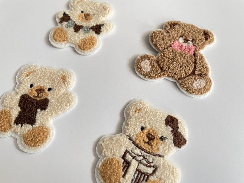 Pode incluir: Quatro patches bordados de ursinhos em v&aacute;rias cores. Dois s&atilde;o creme com detalhes marrons, um com um cachecol. Um &eacute; marrom com um la&ccedil;o rosa. O &uacute;ltimo &eacute; creme com um la&ccedil;o marrom e azul.