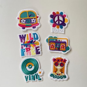Könnte beinhalten: Sechs bestickte Aufnäher mit bunten Motiven: ein gelb-rosa Campingbus, eine mehrfarbige Friedensblume, der Schriftzug "WILD & FREE" mit einer Feder, ein violetter Ghettoblaster, eine türkise Vinylschallplatte und eine Person mit Blumenbrille.