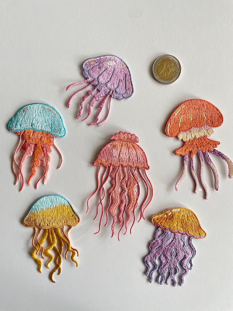 May include: Embroidered jellyfish patches in various colors, including purple, orange, yellow, and blue. Each patch features detailed stitching and flowing tentacles. A Euro coin is also present.