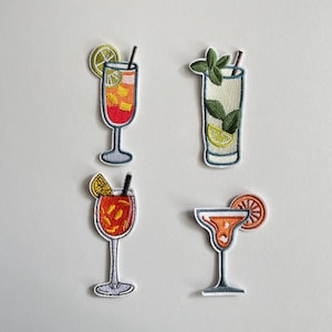 Könnte beinhalten: Vier gestickte Cocktail-Patches. Die Patches zeigen eine Vielzahl von Getränken, darunter eine Margarita, ein Highball mit Minze und zwei weitere Cocktails, die jeweils mit Fruchtscheiben und Strohhalmen garniert sind. Die Patches haben einen weißen Rand.