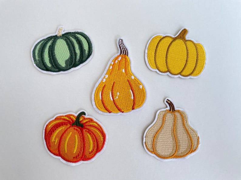 May include: Five embroidered pumpkin patches in various shapes and colors. The patches include a green, yellow, orange, and tan pumpkin designs with white borders. These patches are perfect for fall-themed crafts and decorations.