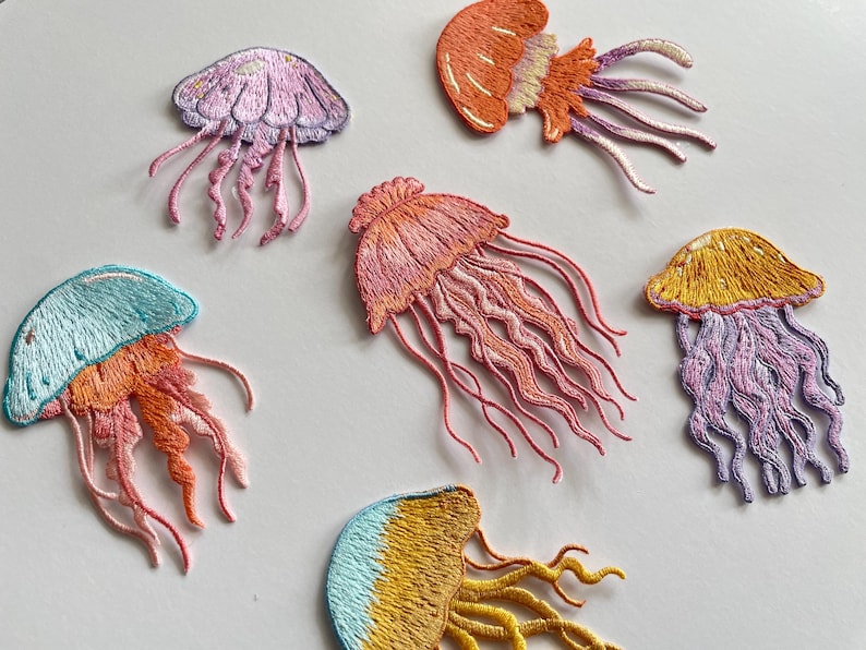 May include: Embroidered jellyfish patches in various colors, including pink, orange, yellow, and blue. Each patch features detailed stitching, with flowing tentacles and a rounded bell shape. These patches are suitable for adding to clothing or accessories.