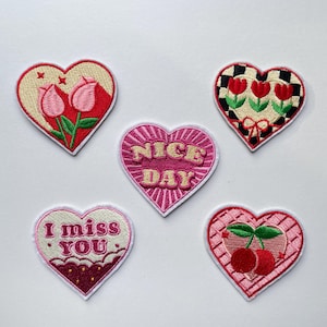 May include: Five heart-shaped embroidered patches. Designs include tulips, cherries, and the phrases "Nice Day" and "I miss you." The patches feature red, pink, and white colors with intricate stitching details.