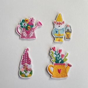 Puede incluir: Cuatro parches bordados con gnomos de jardín y regaderas. Los parches incluyen una regadera rosa con flores, un gnomo sosteniendo una linterna, un gnomo con un sombrero rosa y una regadera amarilla con flores.