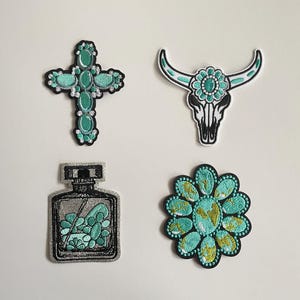 Könnte beinhalten: Vier gestickte Aufnäher mit türkisfarbenen und goldenen Akzenten. Designs umfassen ein Kreuz, einen Stierschädel, eine Parfümflasche und eine Blume. Jeder Aufnäher hat einen schwarzen Rand auf weißem Hintergrund.