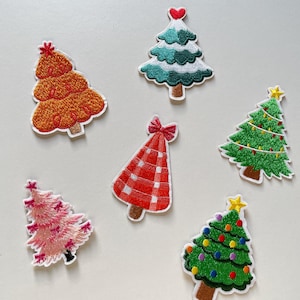 May include: A collection of embroidered Christmas tree patches in various colors and designs. The patches include trees in orange, teal, green, pink, and a red plaid tree. Each tree has a unique embellishment, such as a star or heart.