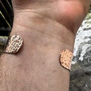 Puede incluir: Una pulsera de pu&ntilde;o de cobre con una textura martillada. El dise&ntilde;o abierto permite un f&aacute;cil uso. La pulsera es de color marr&oacute;n rojizo c&aacute;lido.