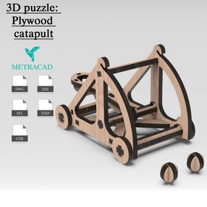 Puede incluir: Rompecabezas 3D de madera de una catapulta con detalles negros y tres pequeñas bolas de madera. El texto "3D puzzle: Plywood catapult" está en la parte superior. El logotipo "METRACAD" también es visible.