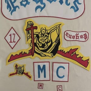 May include: A collection of embroidered patches, including one with the text "Pagan's" in blue gothic script. Other patches feature a figure with a cross, the letters "MC", and the number "1%" in red and white, on a white background.