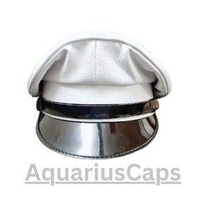 Könnte beinhalten: Weiße Kapitänsmütze mit glänzendem schwarzem Band und Visier. Der Hut hat eine strukturierte Optik und der Text "AquariusCaps" ist unten sichtbar. Ein stilvolles Accessoire.