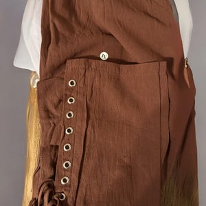 Peut inclure: Pantalon marron avec d&eacute;tails &oelig;illets et chemise blanche. Le pantalon a une &eacute;tiquette de taille moyenne et un cordon de serrage. Le pantalon est en tissu textur&eacute;. La chemise est blanche avec un col haut.