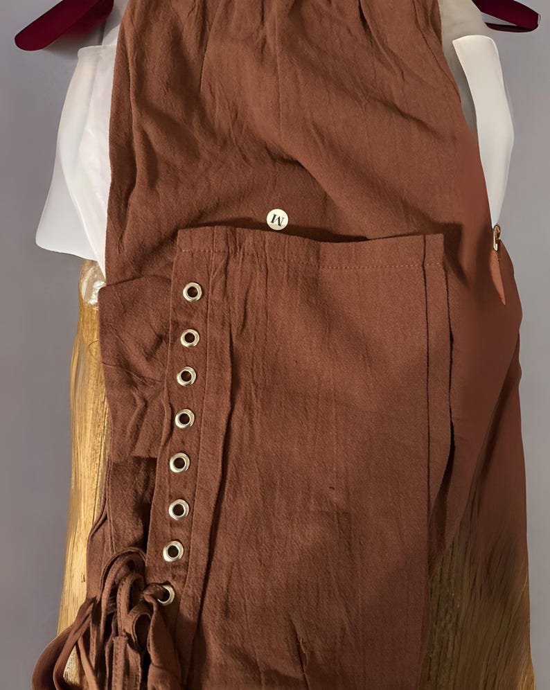 Peut inclure: Pantalon marron avec d&eacute;tails &oelig;illets et chemise blanche. Le pantalon a une &eacute;tiquette de taille moyenne et un cordon de serrage. Le pantalon est en tissu textur&eacute;. La chemise est blanche avec un col haut.