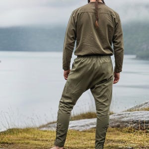 Peut inclure: Un ensemble vert olive compos&eacute; d'une chemise &agrave; manches longues et d'un pantalon assorti. Le pantalon pr&eacute;sente des d&eacute;tails de boutons sur les c&ocirc;t&eacute;s. L'ensemble est en tissu textur&eacute;, &eacute;voquant des v&ecirc;tements historiques ou fantastiques.