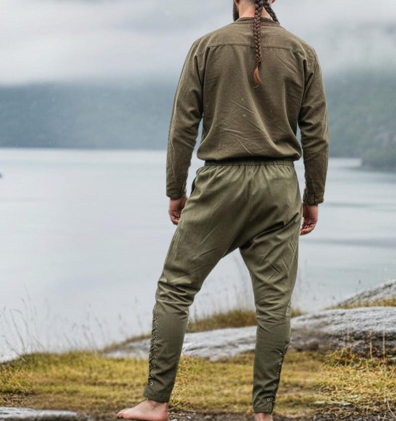 Peut inclure: Un ensemble vert olive compos&eacute; d'une chemise &agrave; manches longues et d'un pantalon assorti. Le pantalon pr&eacute;sente des d&eacute;tails de boutons sur les c&ocirc;t&eacute;s. L'ensemble est en tissu textur&eacute;, &eacute;voquant des v&ecirc;tements historiques ou fantastiques.