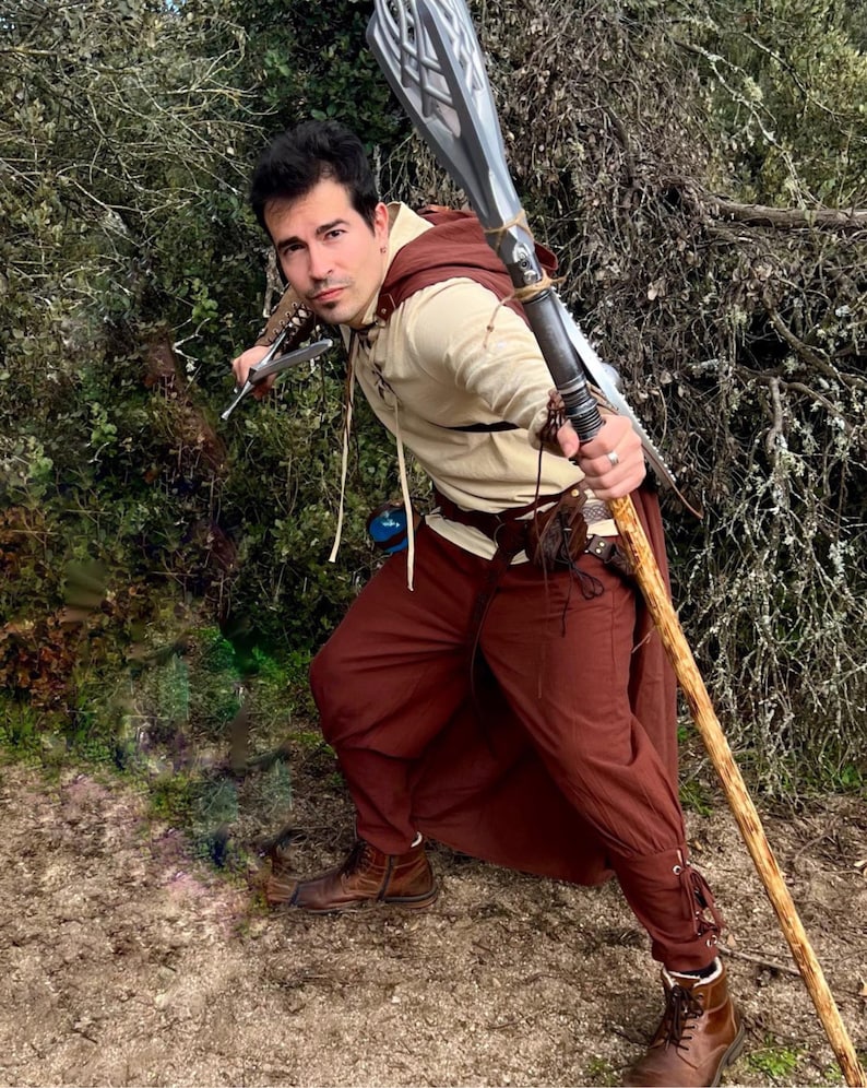 Peut inclure: Une personne en costume fantastique, tenant une lance et une petite lame. La tenue comprend une chemise beige, un pantalon marron, une cape marron et des bottes marron. La lance a une lame argent&eacute;e et un manche en bois.