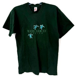 May include: Dark green t-shirt with the text "WAVE DANCER BELIZE" and three turquoise sea turtles embroidered on the front. The shirt is made of a soft material and has a classic crew neck.