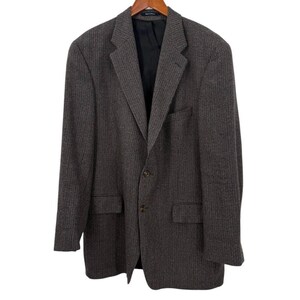 May include: A brown and gray patterned blazer with a notched lapel, two front pockets, and a two-button closure. The blazer is hanging on a wooden hanger against a white background. The interior lining is black.