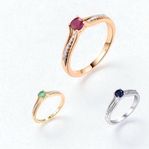 Puede incluir: Tres anillos con piedras preciosas. El anillo superior es de oro rosa con una piedra central de rubí y pequeños diamantes. El segundo anillo es de oro con una piedra central de esmeralda y diamantes. El tercer anillo es de plata con un zafiro y diamantes.