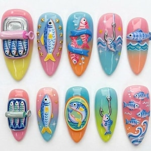 May include: A set of ten press-on nails featuring 3D designs with a fishing theme. The nails display colourful illustrations of sardines in tins, individual fish, fishing hooks, and ocean waves in shades of pink, blue, orange, and yellow.