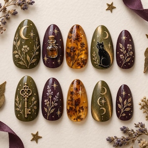 May include: A set of ten almond-shaped press-on nails featuring olive green and deep purple bases with gold foil accents, including illustrations of a crescent moon, a black cat, a vintage key, a small glass potion bottle, and botanical motifs.