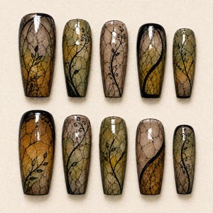 May include: A set of ten press-on nails featuring a gradient of olive green, brown, and gold tones with a subtle glitter finish. Each nail is decorated with a black hand-painted vine motif and a delicate, fine-lined crackle or net pattern overlay.