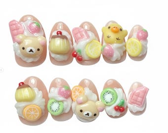 May include: A set of ten artificial nails with a light pink base, each adorned with miniature dessert-themed decorations. Designs include a bear, pudding, chocolate, fruit slices, and whipped cream.