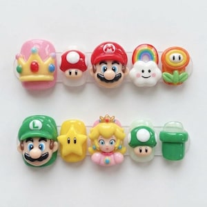 May include: A collection of colorful nail art featuring characters and symbols from the Super Mario video game series. Includes Mario, Luigi, Princess Peach, a mushroom, a star, a rainbow, a flower, and a green pipe.