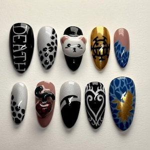 May include: A set of ten artificial nails with various designs. One nail is black with the word "DEATH" in white. Other nails feature patterns like leopard spots, a cat face, a gold emblem, and abstract designs in black, white, gold, and blue.