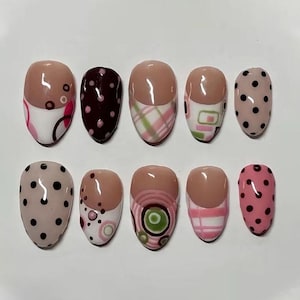 May include: A set of ten artificial nails in various designs. The nails feature a nude base with patterns including polka dots, plaid, and abstract designs in pink, white, and green. Some nails have a brown tip.