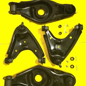 May include: Four black automotive suspension control arms and hardware are arranged on a yellow background. The control arms have a curved shape with bushings and ball joints. Small nuts, bolts, and washers are also visible.