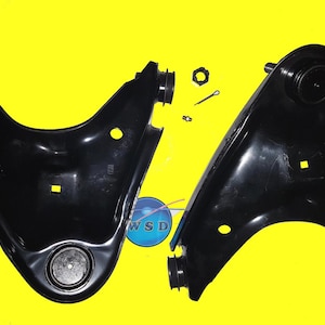 Op de afbeelding: Twee zwarte draagarmen voor auto's met bijbehorende hardware, inclusief moeren, bouten en splitpennen, worden getoond tegen een heldergele achtergrond. De onderdelen zijn nieuw en klaar voor installatie.