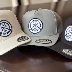 May include: Three baseball caps in cream, gray, and black. Each cap features a circular patch with crossed rifles, stars, and the text "FDT RESIST" in a navy blue and white design. The caps have a snapback closure.