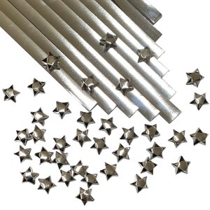 Puede incluir: Un paquete de tiras de papel de origami plateado con un mont&oacute;n de estrellas de origami plateadas esparcidas a su alrededor.