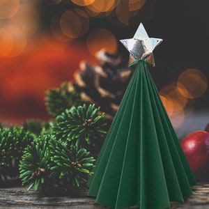 Puede incluir: Un &aacute;rbol de Navidad de papel verde con una estrella plateada en la parte superior. El &aacute;rbol est&aacute; sobre una superficie de madera con ramas de pino y manzanas rojas.