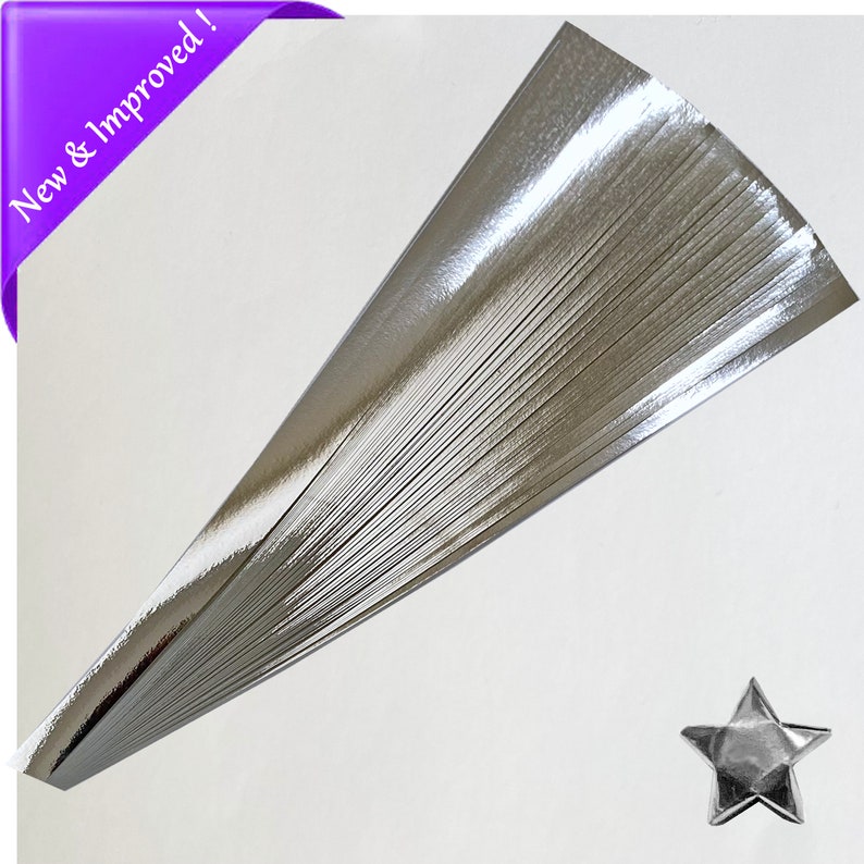 Puede incluir: Una pila de tiras de papel de origami plateado. El papel es brillante y tiene un acabado met&aacute;lico. Una estrella de origami plateada se muestra en la esquina inferior derecha de la imagen.