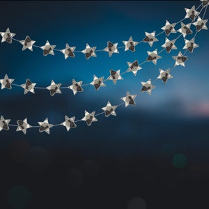 Puede incluir: Una guirnalda de estrellas plateadas con varias hileras de estrellas colgando sobre un fondo azul.
