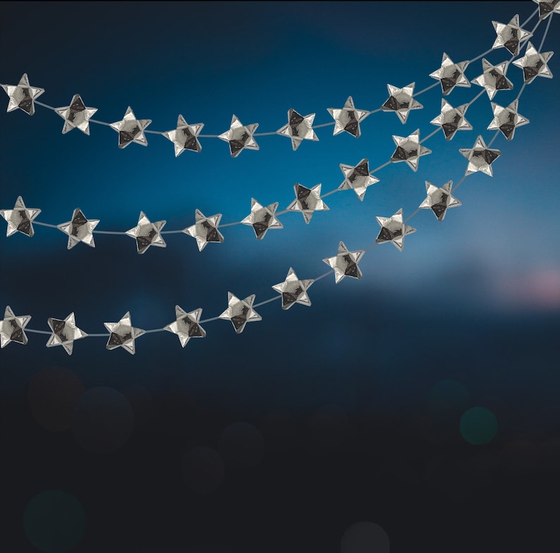 Puede incluir: Una guirnalda de estrellas plateadas con varias hileras de estrellas colgando sobre un fondo azul.