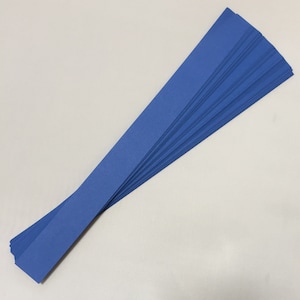 Puede incluir: Una pila de tiras de papel largas y finas de color azul abanicadas sobre una superficie blanca. Las tiras son de un color azul sólido y vibrante y parecen estar hechas de cartulina o un material similar. Las tiras de papel son probablemente para manualidades u otros proyectos creativos.