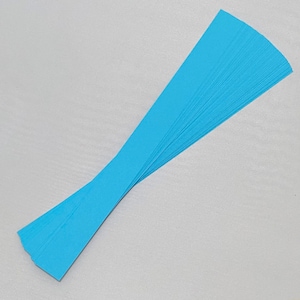 Puede incluir: Un conjunto de tiras de papel azul claro dispuestas en abanico sobre una superficie gris. Las tiras son largas y estrechas, con una ligera curva. El papel tiene una textura suave y un color sólido.