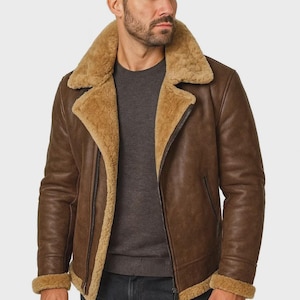 May include: A brown leather jacket with a shearling collar and lining. The jacket has a zip closure and a classic aviator style. The cuffs and collar are lined with a light brown shearling. The jacket is worn over a gray sweater.