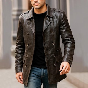 Puede incluir: Chaqueta de cuero marrón oscuro de doble botonadura. La chaqueta tiene un estilo clásico de gabardina con dos filas de botones, cuello con solapas y dos bolsillos delanteros. Se lleva sobre una camiseta negra y vaqueros azules.